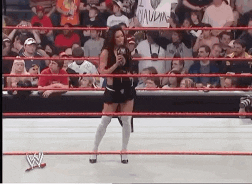 a woman is standing in a wrestling ring holding a microphone in front of a crowd of people .
