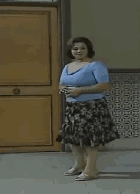 a woman is standing in front of a door wearing a blue shirt and a skirt .