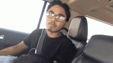 a man is sitting in the back seat of a car wearing glasses and earbuds .