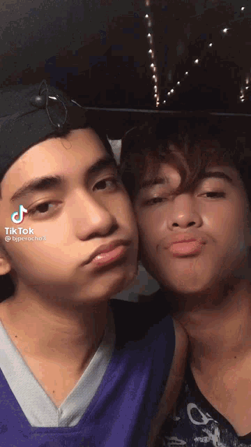 two young men are posing for a picture and one of them is wearing a black hat