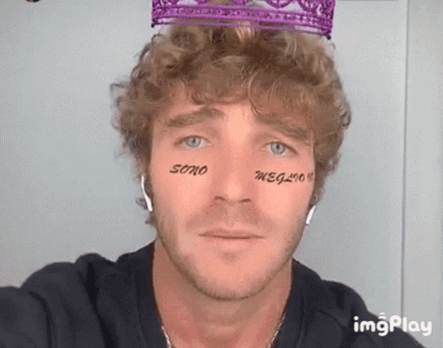 a man with curly hair is wearing a purple crown on his head and has tattoos on his face .
