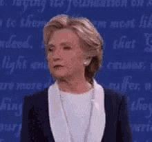 a woman in a suit and white shirt is standing in front of a blue background .