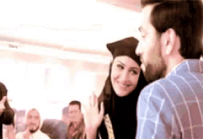 a man and a woman are standing next to each other and the woman is wearing a graduation cap and hijab .
