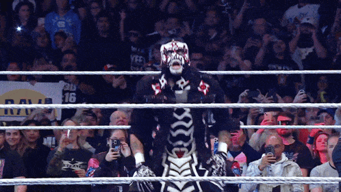 a man in a skeleton costume stands in front of a crowd with a sign that says raw 16