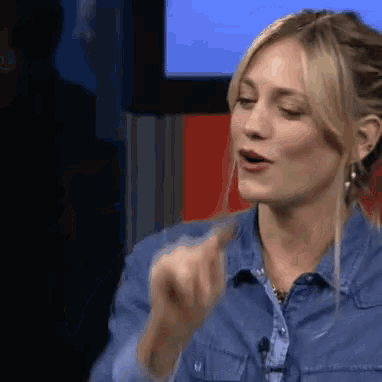 a woman in a denim shirt is talking into a microphone and pointing