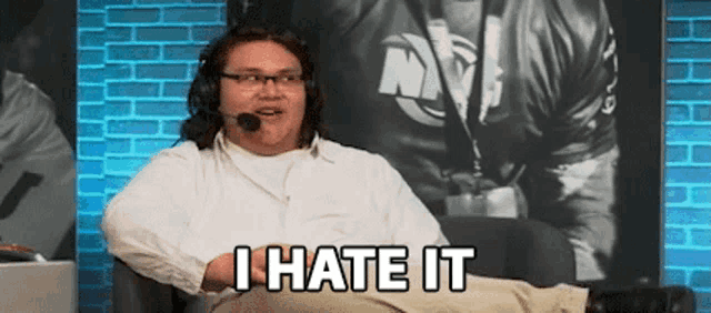 a man wearing a microphone and glasses is sitting in a chair and saying `` i hate it '' .