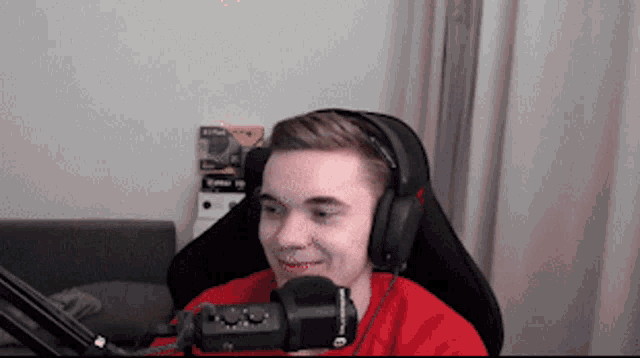 a young man wearing headphones and a red shirt is sitting in front of a microphone and smiling