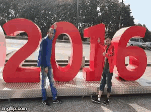 two young boys pose in front of a large red sign that says 2016