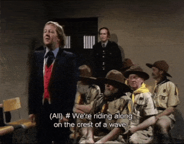a man in a suit and tie stands in front of a group of boy scouts and says " all " #