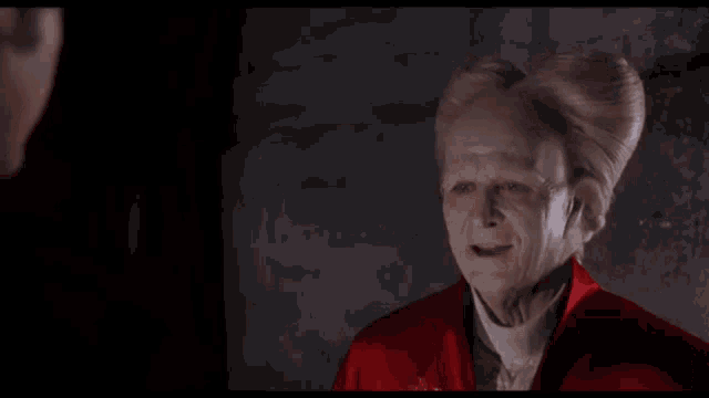 a man with a white head and a red jacket smiles at another man