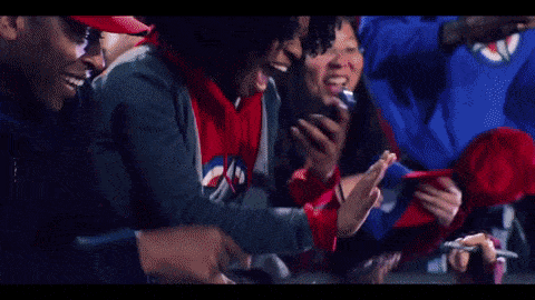 a group of people are sitting in a stadium watching a game and one of them is holding a cell phone .