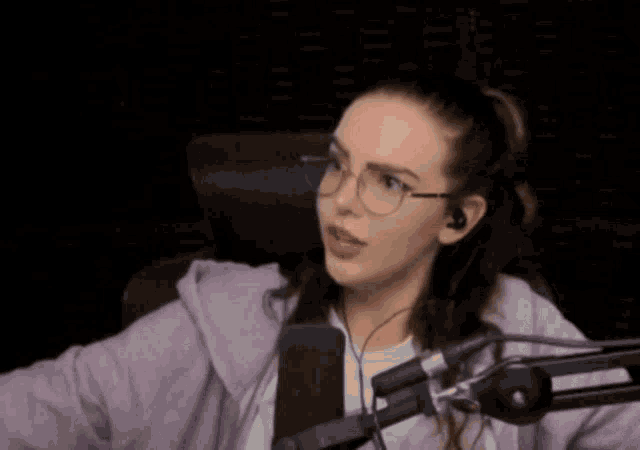a woman wearing glasses and headphones is sitting in front of a microphone in a dark room