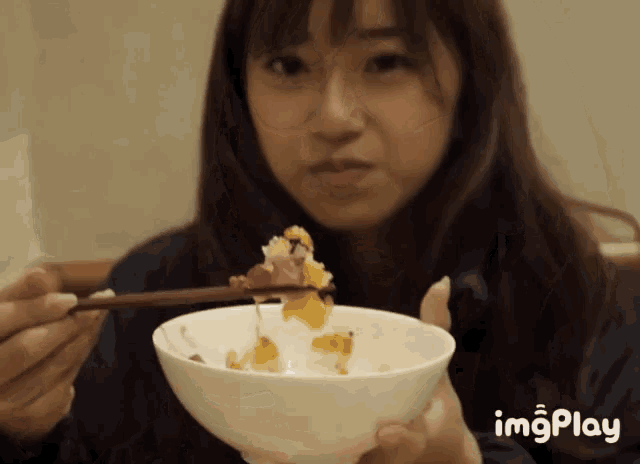 a woman is holding a bowl of food with chopsticks and the word imgplay on the bottom