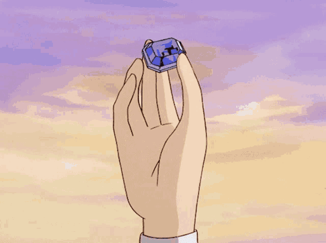 a hand is holding a blue box with a cross on it in front of a cloudy sky