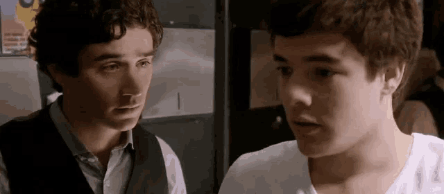 two young men are standing next to each other and one has a poster on the wall that says ' i 'm sorry '