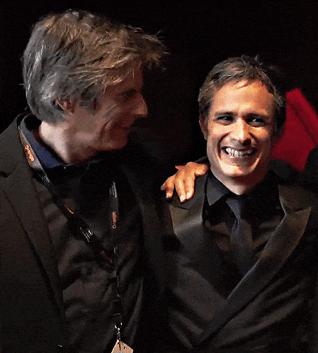 two men in suits are laughing together and one has a lanyard around his neck