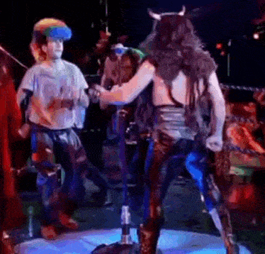 a man in a costume with horns is dancing on a stage while another man stands behind him .