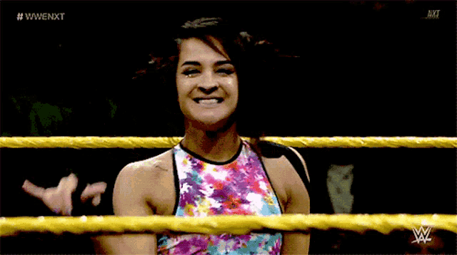 a woman is smiling in a wrestling ring while wearing a colorful top .