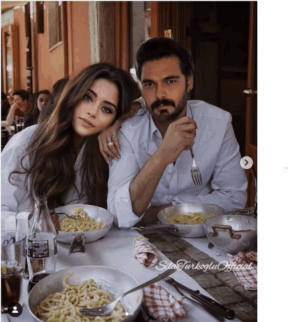 a man and woman are sitting at a table with plates of noodles