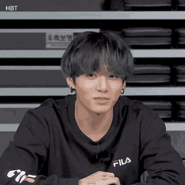 a young man wearing a black fila sweatshirt is sitting at a table