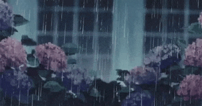 a person is standing in the rain in front of a building with flowers in the background .