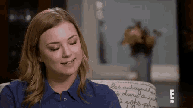 a woman in a blue shirt is sitting in a chair with her eyes closed and smiling .