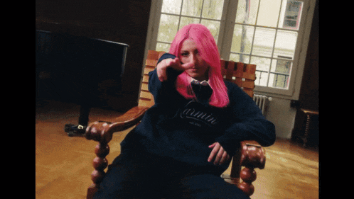 a woman with pink hair is sitting in a chair wearing a black carmin sweatshirt
