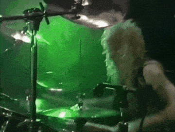 a man playing drums in front of a green light