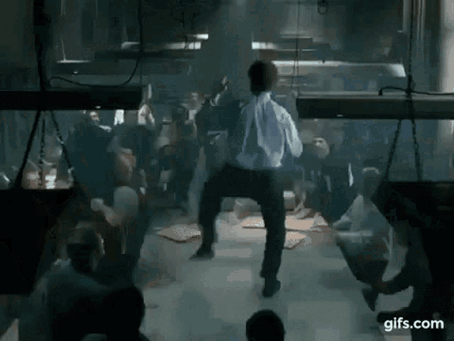 a man in a white shirt is dancing in front of a crowd of people in a dark room .