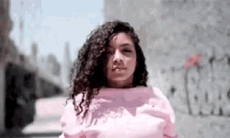 a woman in a pink sweatshirt is standing in front of a wall with graffiti on it that says ' chicago bulls '