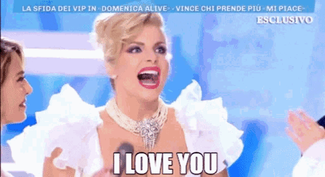 a woman in a white dress says i love you in front of a microphone