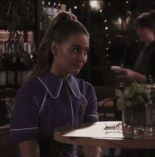 a woman in a blue shirt sits at a table