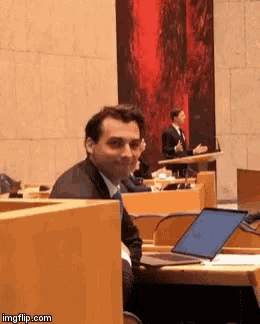 a man in a suit is sitting at a desk with a laptop in front of him in a conference room ..