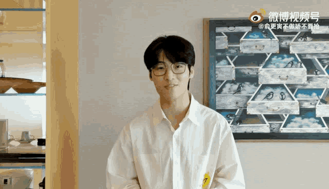 a man wearing glasses and a white shirt is standing in front of a painting in a room