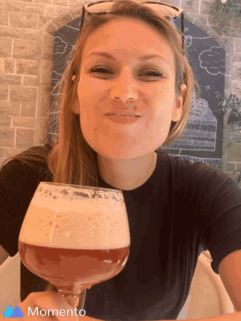 a woman is holding a glass of beer and the word momento is on the bottom right