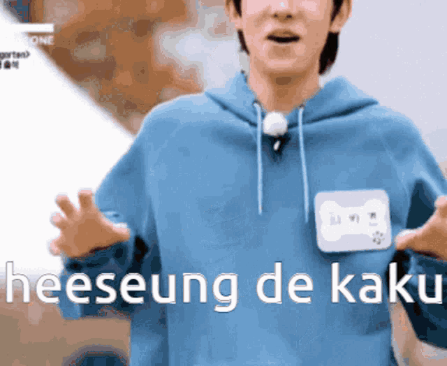 a man in a blue hoodie with a name tag that says heeseung de kaki on it