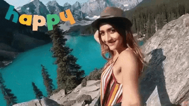 a woman in a hat is standing on a rock near a lake .
