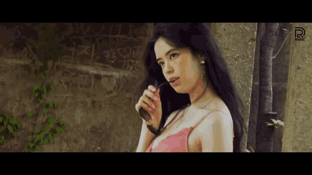 a woman in a pink top stands in front of a wall with graffiti on it that says music
