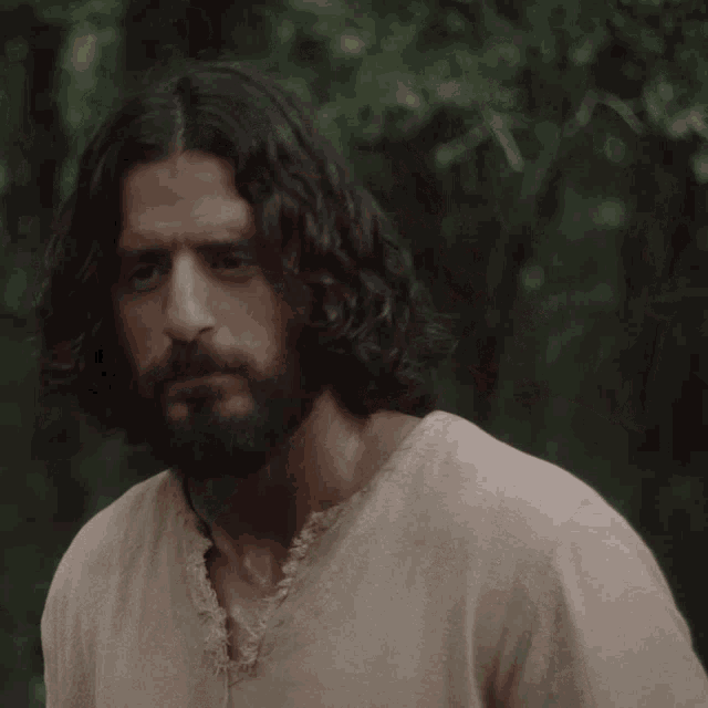 a man with long curly hair and a beard wears a tan shirt