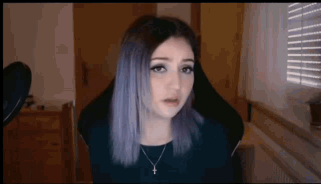 a girl with purple hair and a cross necklace is sitting in front of a microphone in a room .