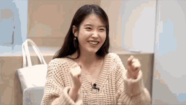 a woman in a sweater is smiling and holding her hands up