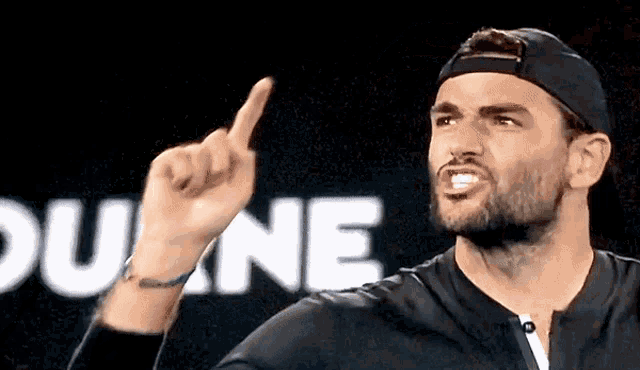 a man wearing a baseball cap is pointing up with his finger