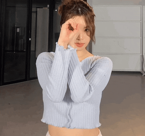 a woman wearing a light blue sweater is making a peace sign