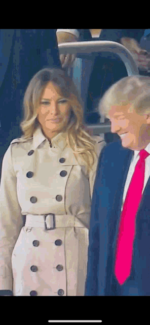 a woman in a trench coat stands next to a man in a suit and pink tie