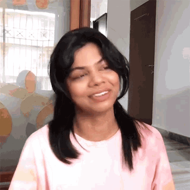 a woman wearing a pink t-shirt is smiling and looking at the camera