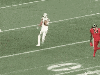 two football players in red uniforms are running on a field . one has the number 11 on his jersey .