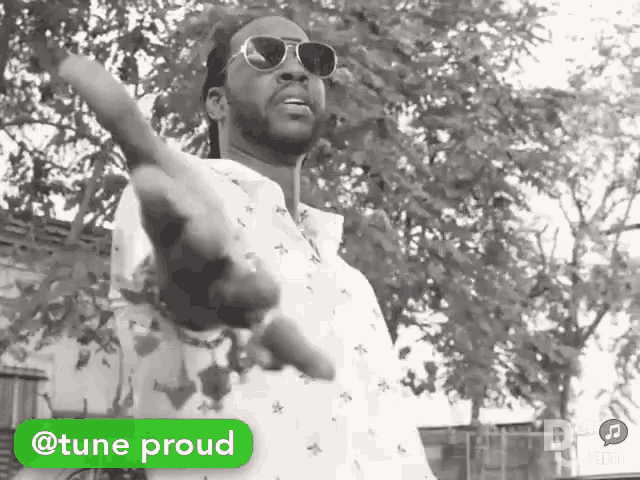 a black and white photo of a man wearing sunglasses and a white shirt with a green sticker that says tune proud