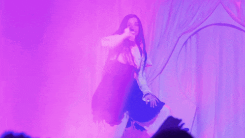 a woman in a black and white dress is dancing in front of purple lights