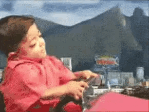 a child in a red shirt is playing with a toy car steering wheel