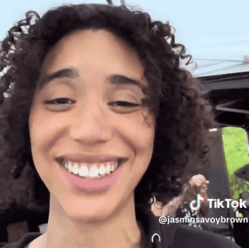 a woman with curly hair is smiling and has a tiktok sticker on her face